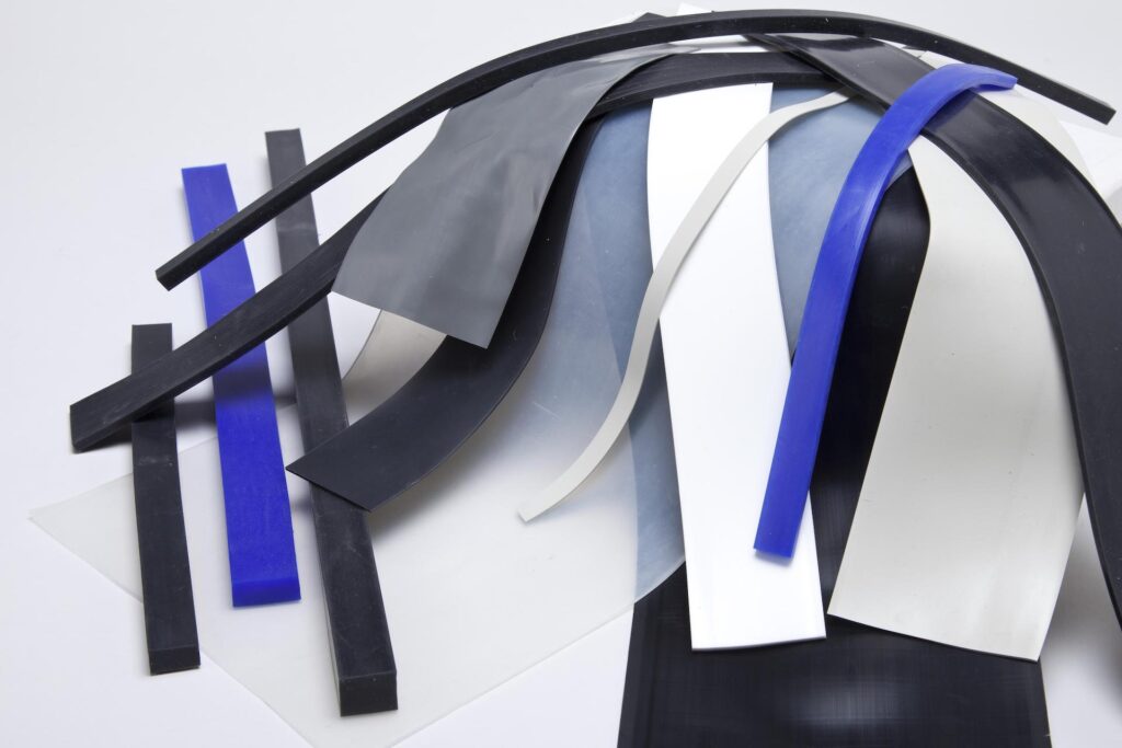 Silicone Rubber Strips 4.min - Silicone Rubber Strips - Viking Extrusions Different types of silicone rubber strips in blue, white, grey and black, stacked on top of each other.